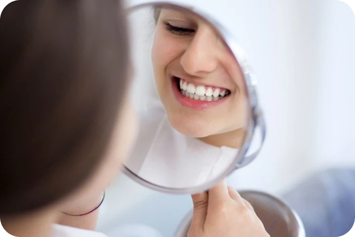 Femme souriante se regardant dans un miroir après un traitement orthodontique